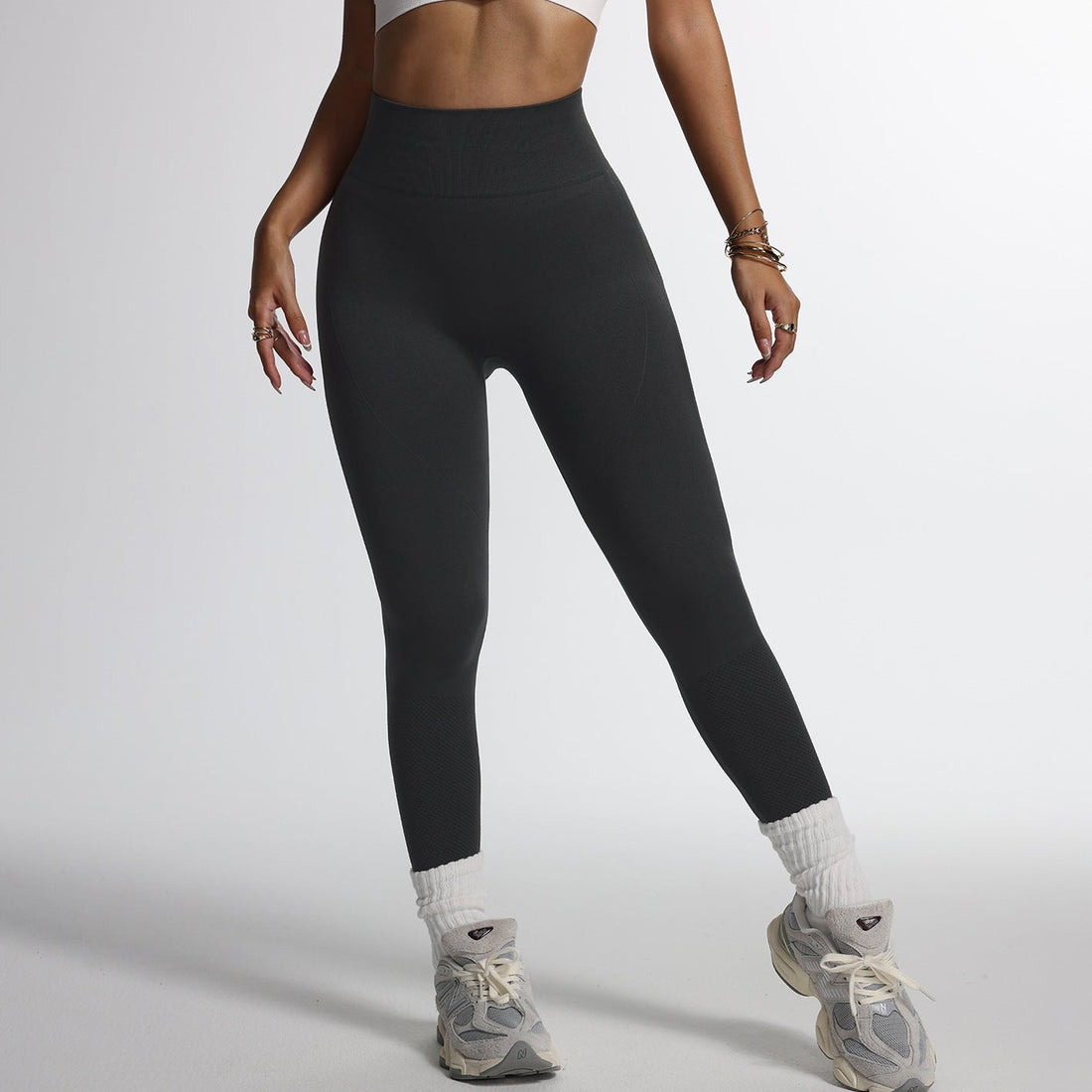 Woman wearing a sleek black activewear onesie, striking a confident fitness pose in a bright modern studio, highlighting seamless fit and versatility.